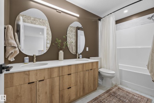 Dual vanity with wood-finish cabinetry, white countertops, and contemporary organic-shaped mirrors - 20907 131 Avenue, Edmonton, AB 