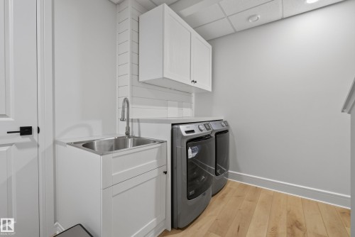 Laundry area featuring light wood-finish flooring, white shaker-style cabinetry, a stainless steel utility sink with a gooseneck faucet, and white shiplap-style wall paneling - 20907 131 Avenue, Edmonton, AB 