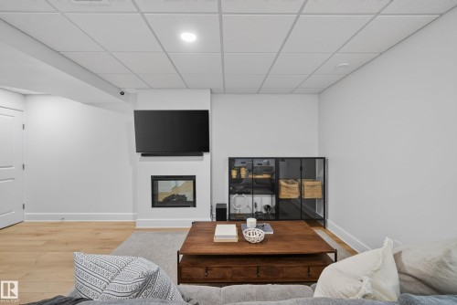 Living area featuring a sleek built-in fireplace, a mounted television, wood-finish flooring, recessed lighting, and a drop ceiling - 20907 131 Avenue, Edmonton, AB 