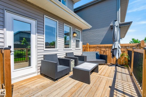 Expansive wood-finish deck featuring a full-light door, multiple windows, an exterior wall light fixture, and a wood privacy fence - 20907 131 Avenue, Edmonton, AB 