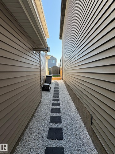 Side yard featuring a gravel pathway with square stepping stones, bordered by vertical vinyl siding - 20907 131 Avenue, Edmonton, AB 