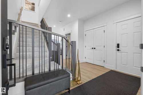 Entryway featuring light wood-finish flooring, white paneled doors, and a staircase with carpeted treads and black metal balusters - 20907 131 Avenue, Edmonton, AB 
