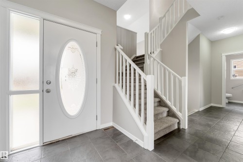 Entryway featuring a white door with an oval etched glass insert, frosted sidelight, and dark gray tile flooring - 3449 28 Street, Edmonton, AB 