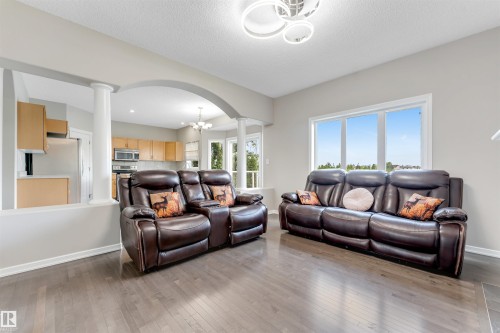 Spacious living area featuring wood-finish flooring, large windows, and a contemporary ceiling fixture - 3449 28 Street, Edmonton, AB 