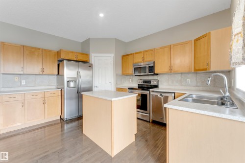 Kitchen featuring wood-finish flooring, light wood cabinetry, white countertops, tile backsplash, and stainless steel appliances - 3449 28 Street, Edmonton, AB 