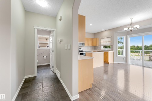 Open-concept living space with wood-finish flooring, a kitchen featuring light wood cabinetry and light countertops, and a dining area with a chandelier - 3449 28 Street, Edmonton, AB 
