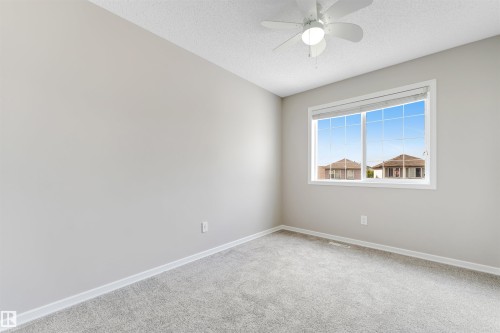 Spacious room featuring light gray carpeting, a large window with white trim, and a white ceiling fan - 3449 28 Street, Edmonton, AB 
