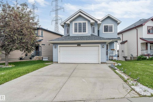 Light blue siding exterior featuring a multi-pane window configuration, attached garage, concrete driveway, and front entry porch with white railings - 3449 28 Street, Edmonton, AB 