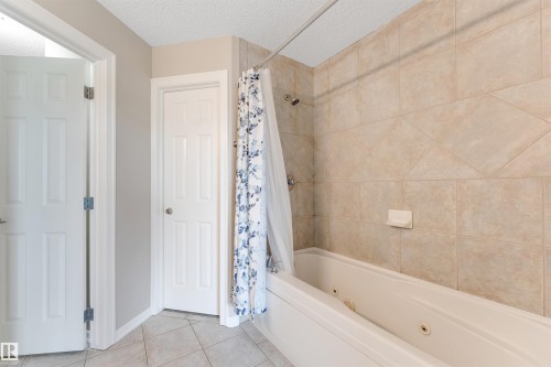 Bathroom featuring a jetted tub with tiled surround, beige wall tiles with a diamond accent pattern, and light-colored floor tiles - 3449 28 Street, Edmonton, AB 