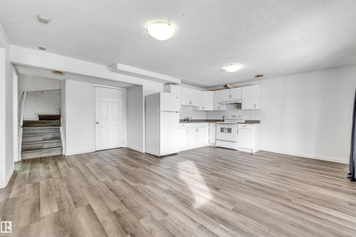 Open-concept living space featuring wood-finish flooring, a white kitchen with granite-look countertops, white appliances, and ample white cabinetry - 3449 28 Street, Edmonton, AB 