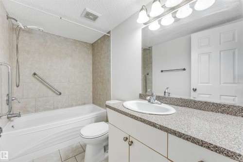 Bathroom featuring a built-in tub with tile surround, a single vanity with a solid surface countertop, and white cabinetry - 3449 28 Street, Edmonton, AB 