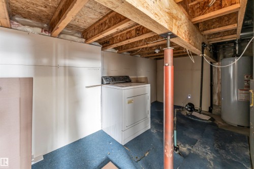 Utility area featuring exposed wood ceiling joists, partial drywall installation, a white clothes dryer, and a water heater - 3449 28 Street, Edmonton, AB 