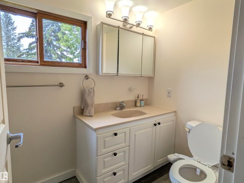 Bathroom featuring a wood-framed window, white vanity with integrated sink, light-colored countertop, and a mirrored medicine cabinet. - 4806 50 Avenue, Elk Point, AB 
