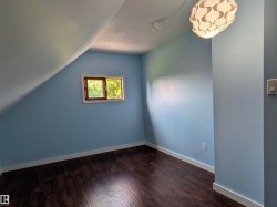 Room with an angled ceiling featuring wood-finish flooring, a window with natural light, and a contemporary ceiling light fixture. - 