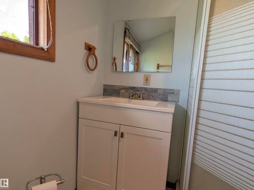 Bathroom vanity featuring a white cabinet with brushed nickel hardware, an integrated sink, a light-toned countertop, and a gray-toned tile backsplash. - 4806 50 Avenue, Elk Point, AB 