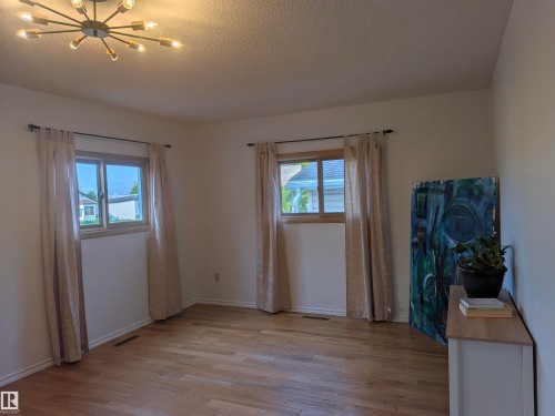Spacious room featuring wood-finish flooring, two large windows with natural wood frames, and a modern sputnik-style ceiling light fixture. - 4806 50 Avenue, Elk Point, AB 