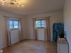Spacious room featuring wood-finish flooring, two large windows with natural wood frames, and a modern sputnik-style ceiling light fixture. - 