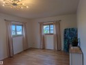 Spacious room featuring wood-finish flooring, two large windows with natural wood frames, and a modern sputnik-style ceiling light fixture. - 4806 50 Avenue, Elk Point, AB 