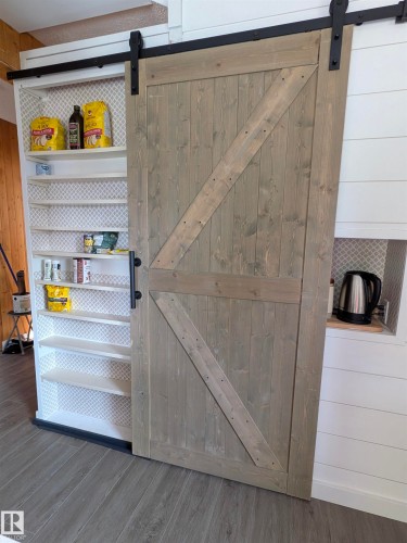 Sliding barn door with dark hardware, offering access to built-in shelving. - 4806 50 Avenue, Elk Point, AB 