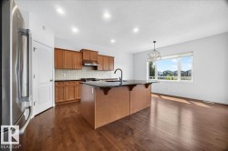 Open-concept kitchen and dining area featuring rich wood-finish flooring, a large island with dark countertop, warm wood cabinetry, and stainless steel appliances - 