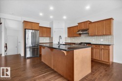 Kitchen featuring a large island with black countertop, stainless steel appliances, wood-finish flooring, recessed lighting, and ample cabinetry - 