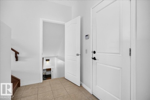 Entryway featuring durable tile flooring, a paneled door with matte black hardware, and a staircase with a wood handrail - 8508 218 Street, Edmonton, AB 