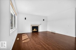 Spacious living area featuring wood-finish flooring, a white-framed window, and a fireplace with a stone surround and white mantel - 