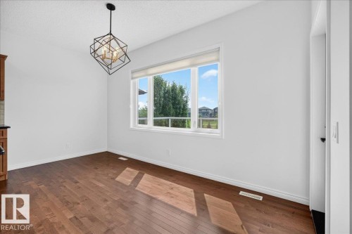 Spacious room featuring wood-finish flooring, white walls, and a contemporary chandelier - 8508 218 Street, Edmonton, AB 