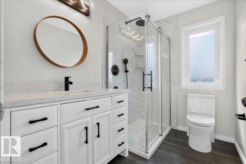 Contemporary bathroom featuring a white vanity with a light-toned countertop, a black matte faucet, and a circular mirror - 8508 218 Street, Edmonton, AB 