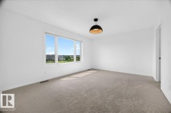 Spacious room with light neutral carpeting, white walls, and a modern black pendant light fixture - 