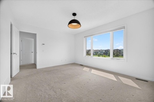 Spacious room featuring a multi-pane window, neutral-toned carpeting, a modern flush-mount light fixture, white walls, and a white interior door - 8508 218 Street, Edmonton, AB 