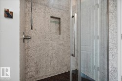Shower with speckled wall tile, brushed nickel fixtures, a built-in shelf, and a frameless glass enclosure with a stainless steel handle - 