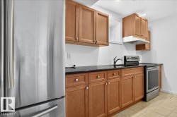 Kitchen featuring wood-finish cabinetry, black countertops, stainless steel appliances, and tile flooring - 