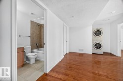 Spacious interior with wood-finish flooring, a stacked washer and dryer unit, a full bathroom with a tiled shower surround, a white bathtub, and a vanity with a light-toned countertop - 