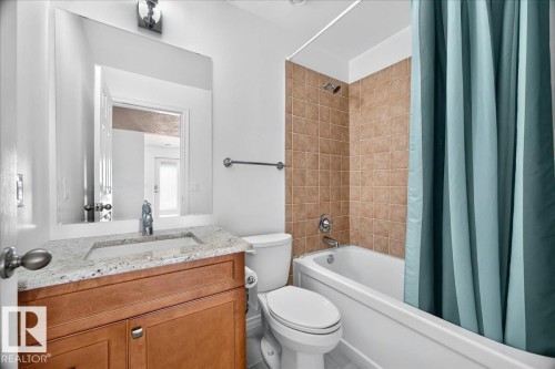 Bathroom featuring a wood-finish vanity with a light-toned countertop, an integrated sink, and a large wall-mounted mirror - 8508 218 Street, Edmonton, AB 