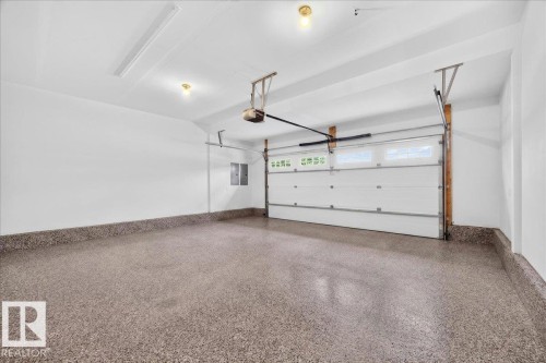 Spacious two-car garage featuring a speckled epoxy floor, white paneled garage door with upper windows, and an automatic garage door opener - 8508 218 Street, Edmonton, AB 