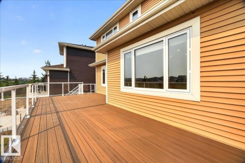Spacious exterior deck featuring wood-finish composite decking, clear panel railings with white posts, and a large multi-pane window - 8508 218 Street, Edmonton, AB 