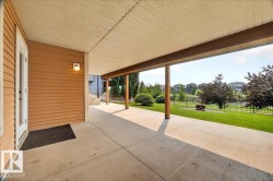 Covered patio with concrete flooring, wood siding, and white trim, featuring a fenced grassy area - 