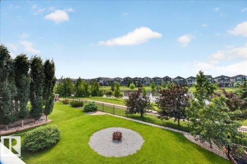 Expansive backyard featuring a manicured lawn, established trees, a circular gravel fire pit area, and a black metal fence - 8508 218 Street, Edmonton, AB 