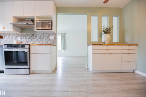 Contemporary kitchen featuring light wood-finish flooring, white cabinetry with gold-tone pulls, stainless steel appliances, and a mosaic tile backsplash - 3531 46 Street, Edmonton, AB 