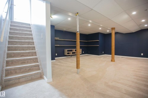 Carpeted stairs leading to a spacious room featuring navy blue walls, light beige carpeting, recessed lighting, and built-in shelving - 3531 46 Street, Edmonton, AB 