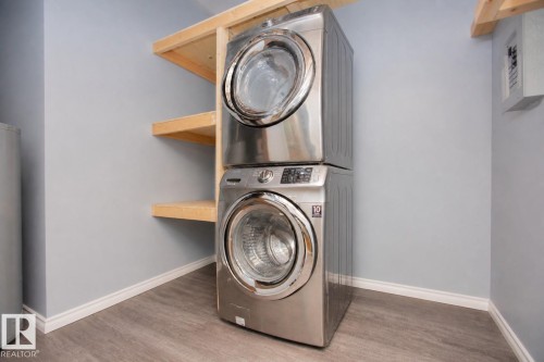 Stackable laundry appliances with front-loading design, complemented by wood shelving and wood-finish flooring - 3531 46 Street, Edmonton, AB 