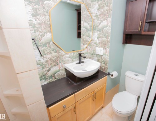 Bathroom featuring a vessel sink with a dark-finish faucet, a gold-framed octagonal mirror, a wood-finish vanity with cabinet storage, and a white toilet - 3531 46 Street, Edmonton, AB 