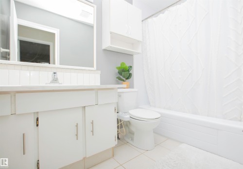 Bathroom featuring white floor tile, a white vanity with cabinet storage, a white bathtub with a shower curtain, and a wall-mounted cabinet - 3531 46 Street, Edmonton, AB 