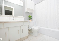 Bathroom featuring white floor tile, a white vanity with cabinet storage, a white bathtub with a shower curtain, and a wall-mounted cabinet - 