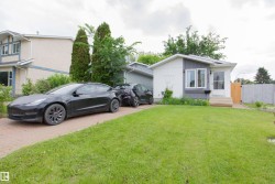 Modern bungalow exterior featuring white and gray siding, a prominent front lawn, a paved driveway, and a wooden fence - 