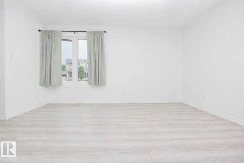Bright room featuring a large window, light wood-finish flooring, white walls, and white baseboards - 3531 46 Street, Edmonton, AB 