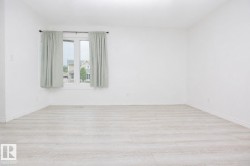 Bright room featuring a large window, light wood-finish flooring, white walls, and white baseboards - 