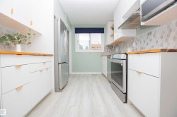 Contemporary kitchen featuring white cabinetry with gold-tone hardware, wood-finish countertops, stainless steel appliances, a patterned tile backsplash, and light wood-finish flooring - 