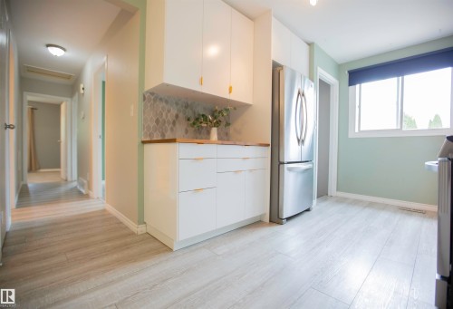 Kitchenette featuring contemporary white cabinetry with gold-tone hardware, a wood-finish countertop, and a decorative tile backsplash - 3531 46 Street, Edmonton, AB 